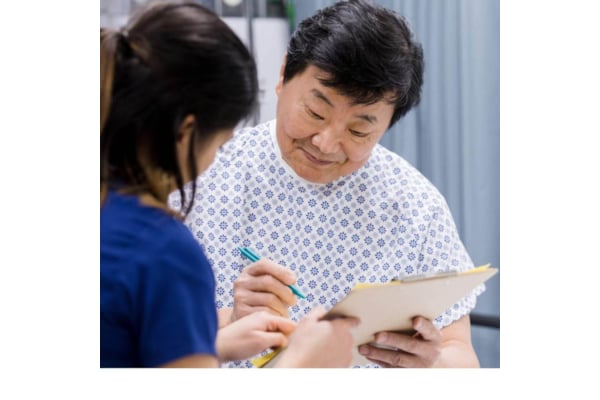 Asian lady in gown signs paperwork with female doctor